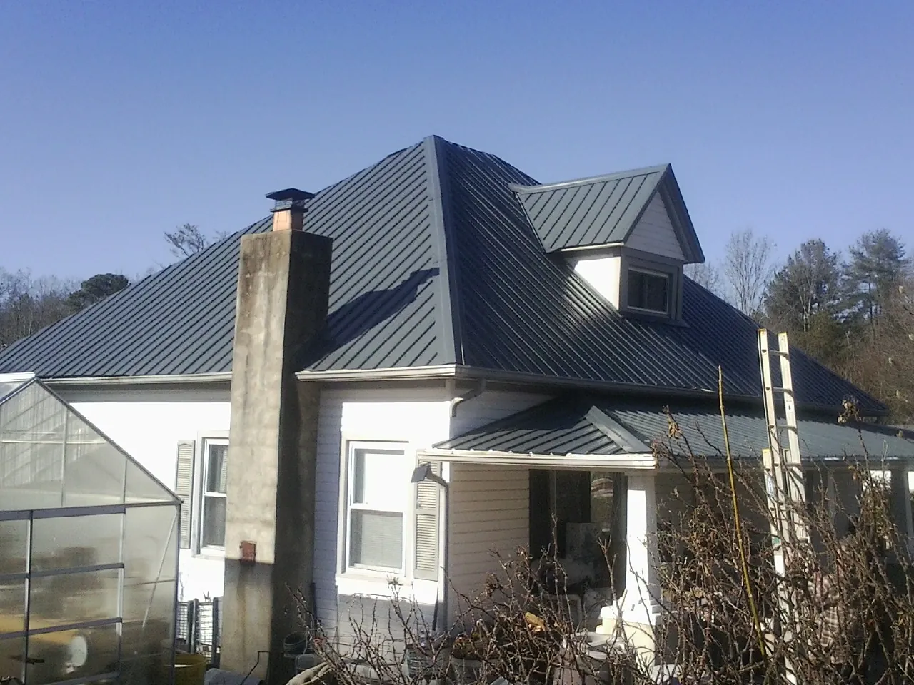 Dark blue standing seam metal roof on a white farmhouse with dormer — Slate & Tile Roof Repair by Roofing Brothers in Islip
