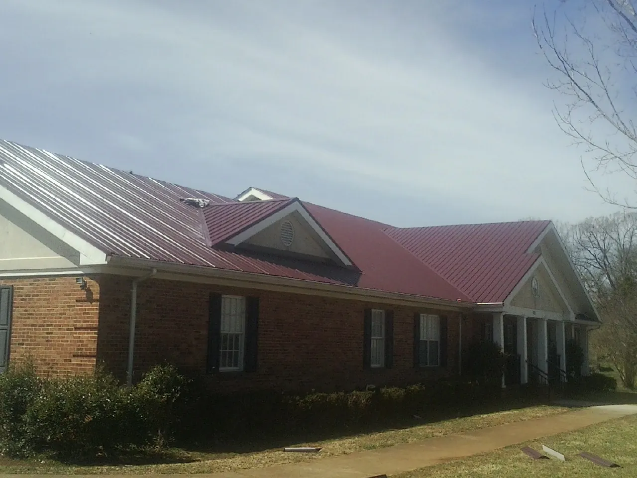 Red metal roof with gabled entries on a long brick building, from a Hail Damage Roof Repair job in Islip