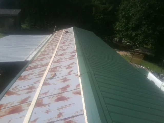 Old rusted panels beside newly installed green metal roofing — Wind Damage Roof Repair by Roofing Brothers in Islip