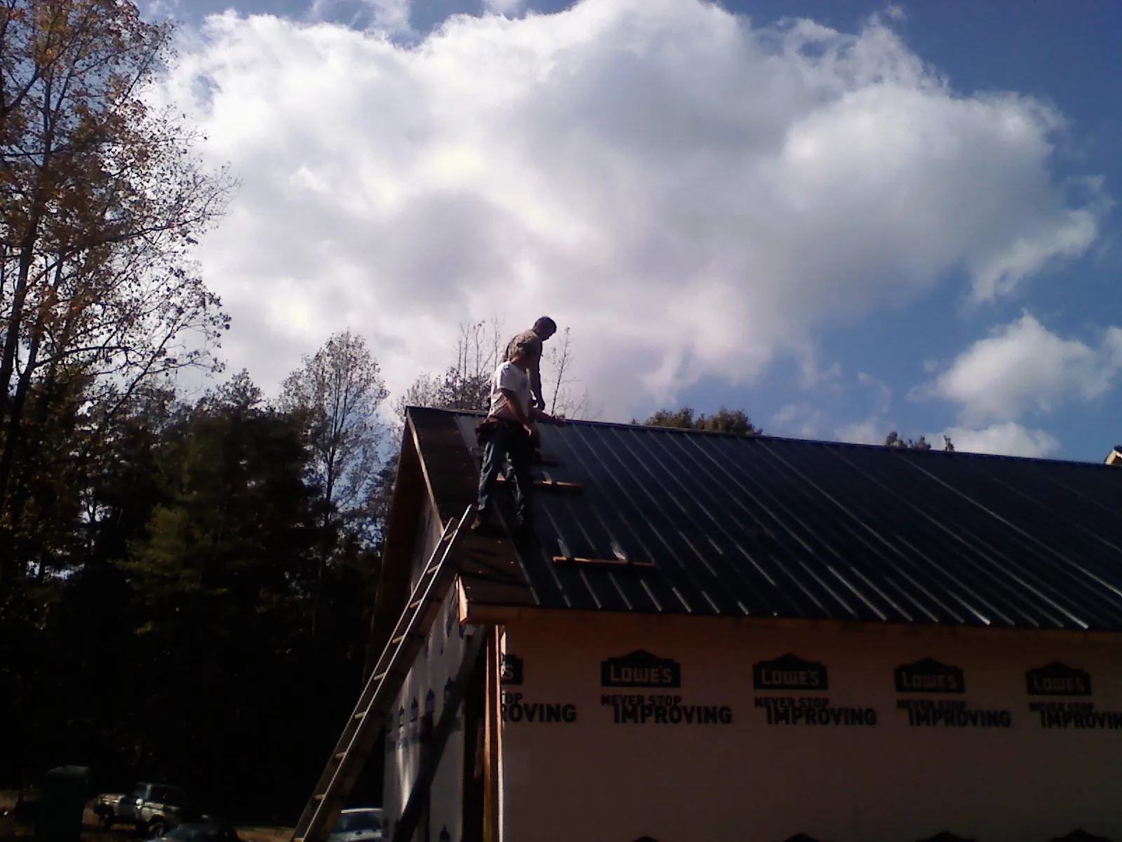 Roofer fastening dark metal panels high against a cloudy sky, from a Roof Inspection job in Islip