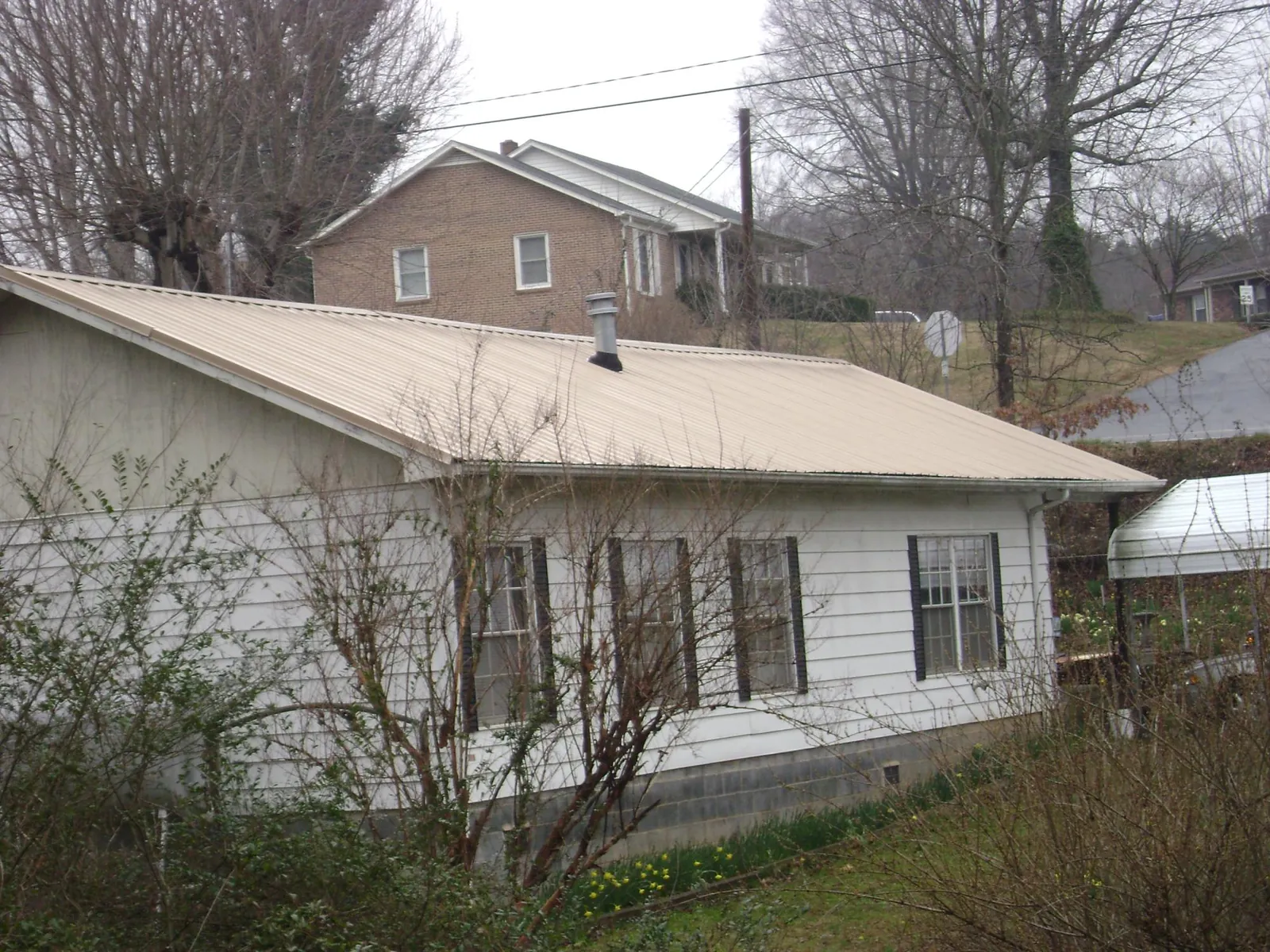 Tan metal roof on a white sided house set into a hillside — Commercial Roofing by Roofing Brothers in Islip