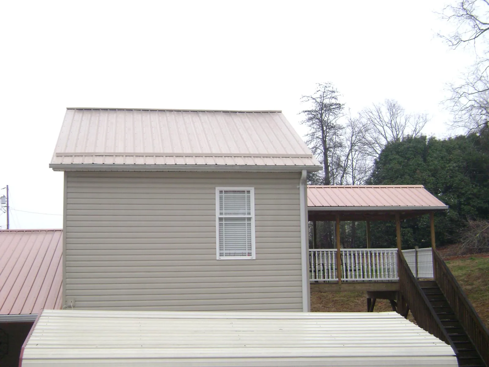 Tan metal roofs on a two story addition and attached porch, from a Roof Replacement job in Islip