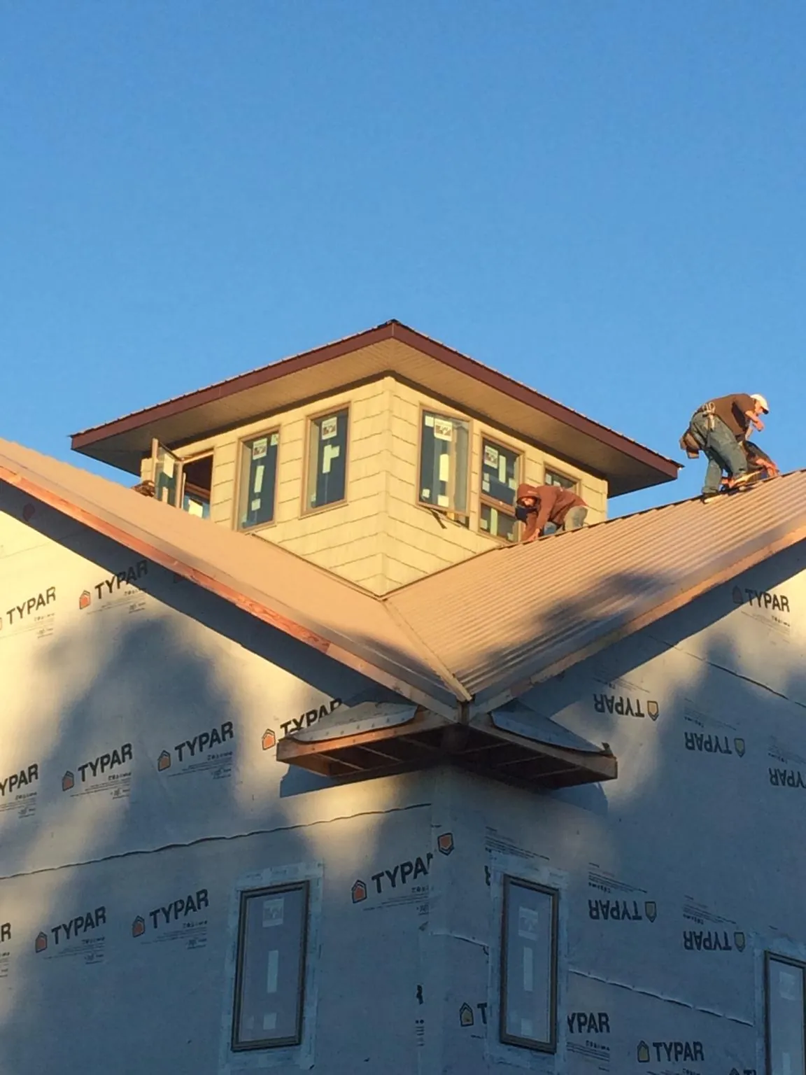 Roofers working around a rooftop cupola on a new metal roof at sunset — Roof Waterproofing in Islip by Roofing Brothers